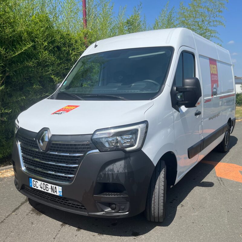 Camionnette Renault blanche stationnée devant des arbres.